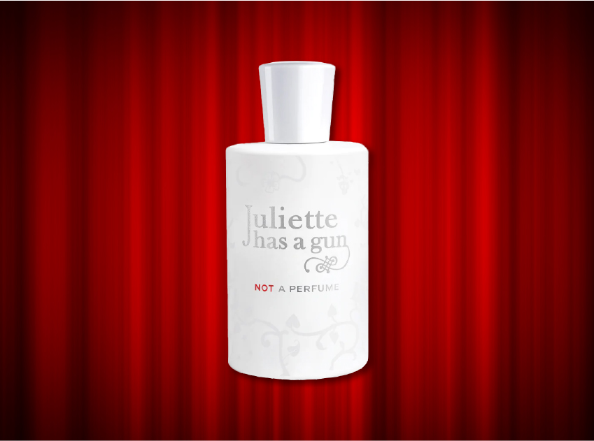 bottle of not a perfume by juliette has a gun in front of red curtains
